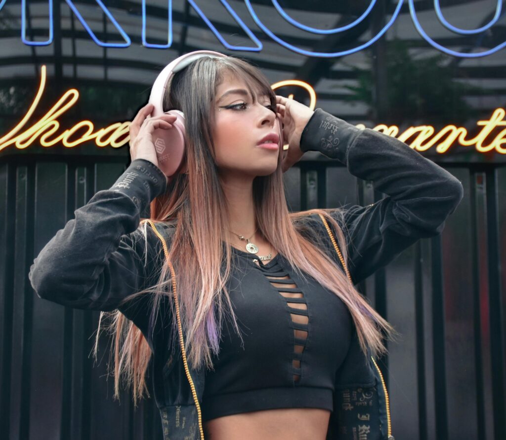 Stylish woman wearing pink headphones, enjoying music in an urban setting with neon lights.