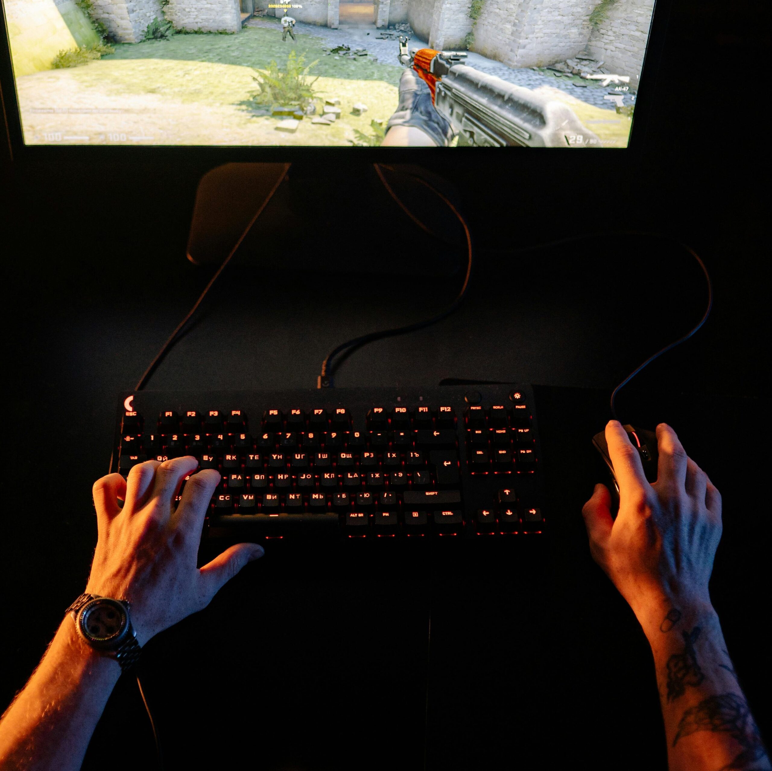 A gamer intensely playing a first-person shooter game on a computer setup indoors at night.